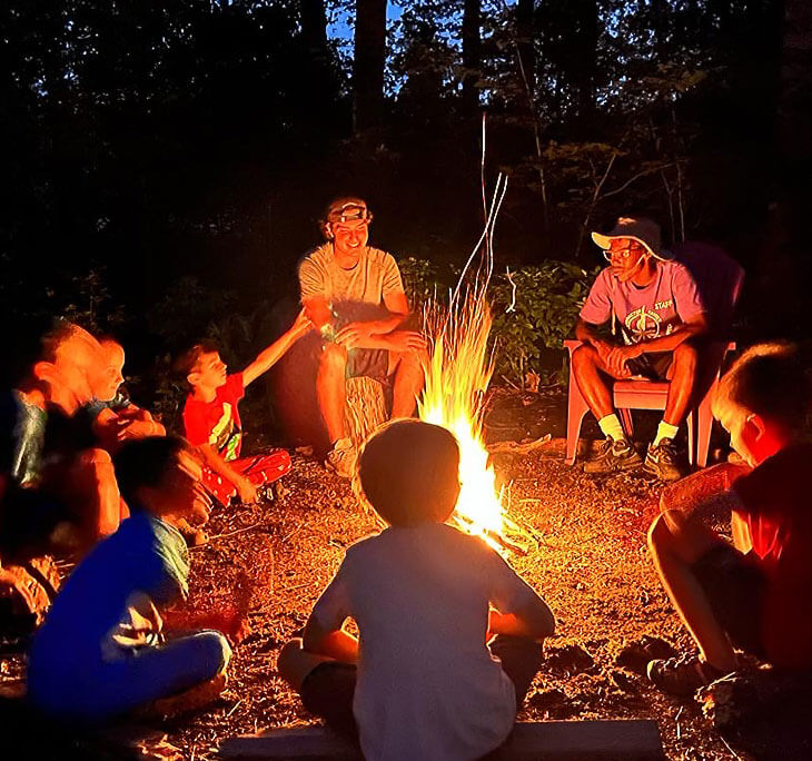 Campers and staff sitting around a campfire at night